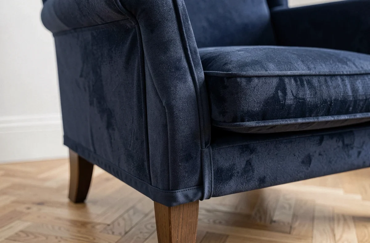 Gros plan sur l'ourlet élastiqué d'une housse extensible bleu marine ajustée sur un fauteuil à oreilles en parquet chêne