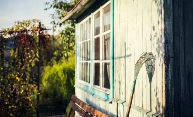 garden rake leaning on white wooden wall at daytime