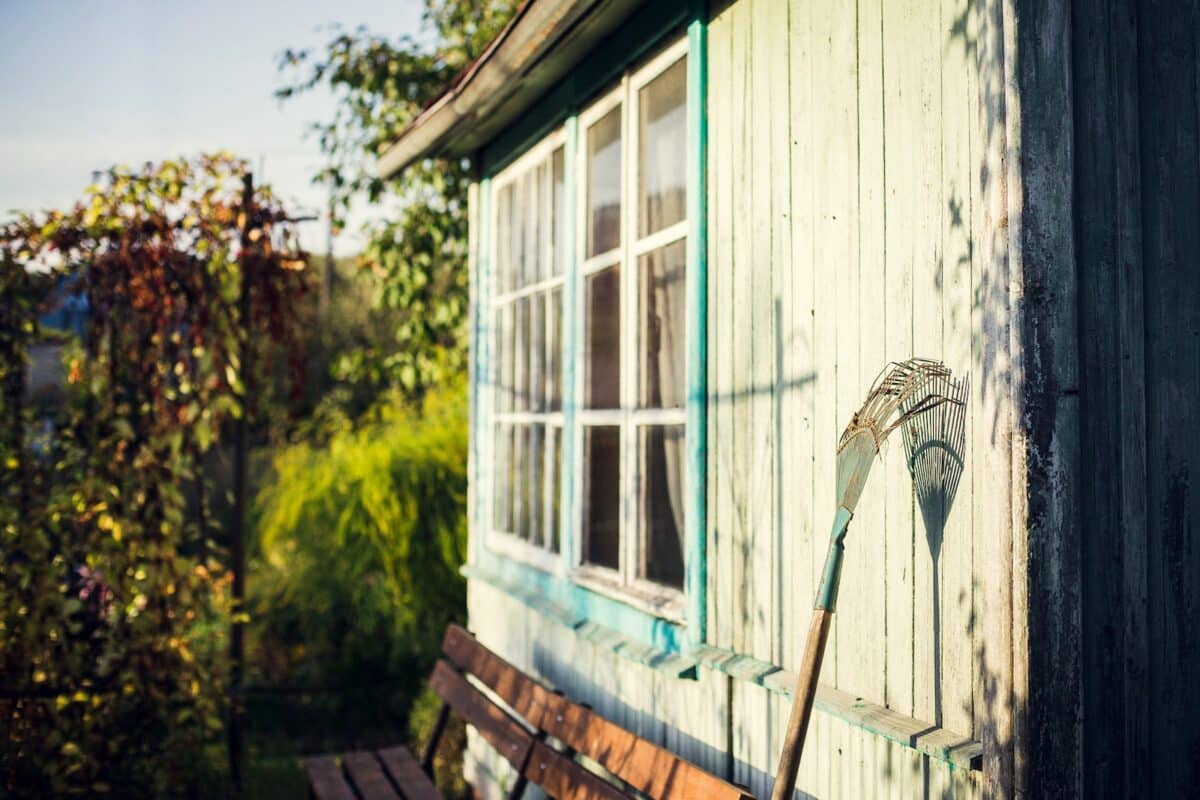 garden rake leaning on white wooden wall at daytime